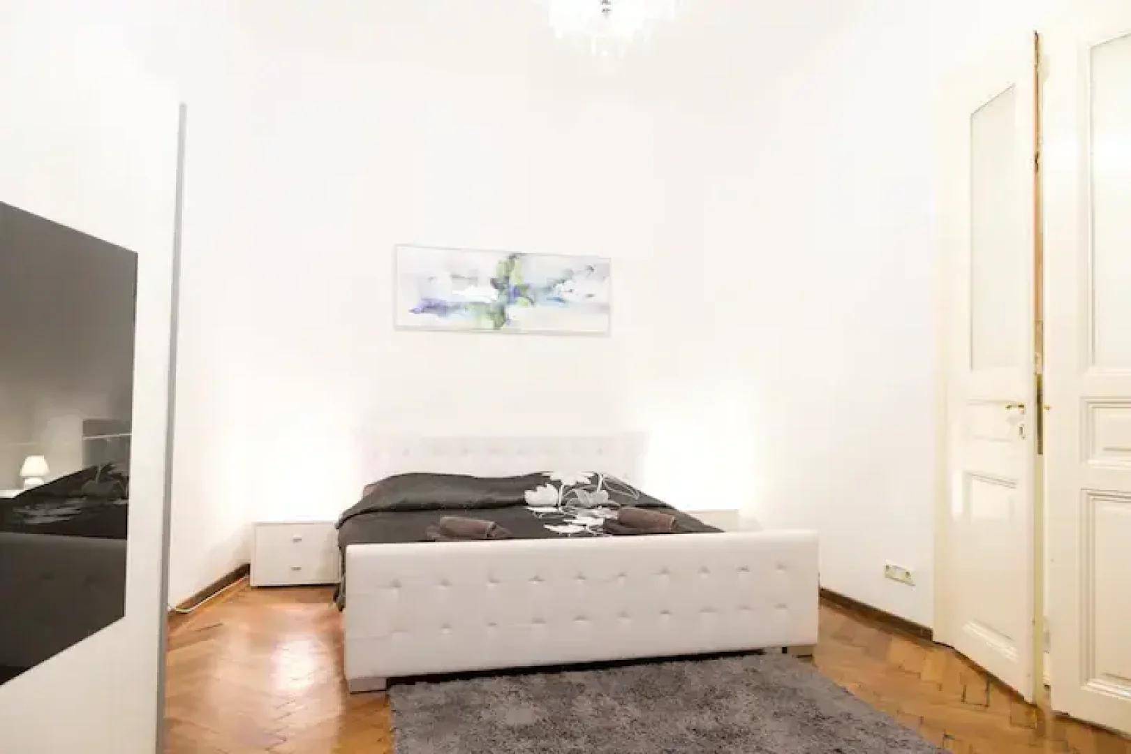 Helles Schlafzimmer mit weißem Bett, Nachttischen und Parkettboden, mit einer Kunst an der Wand.