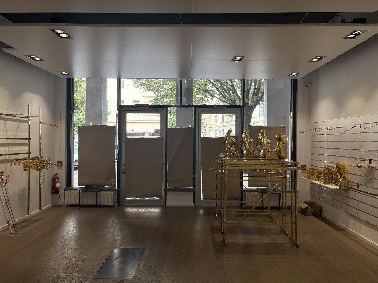 Verkaufsraum mit großen Schaufenstern, teilweise verdeckt, und goldenen Kleiderständern.