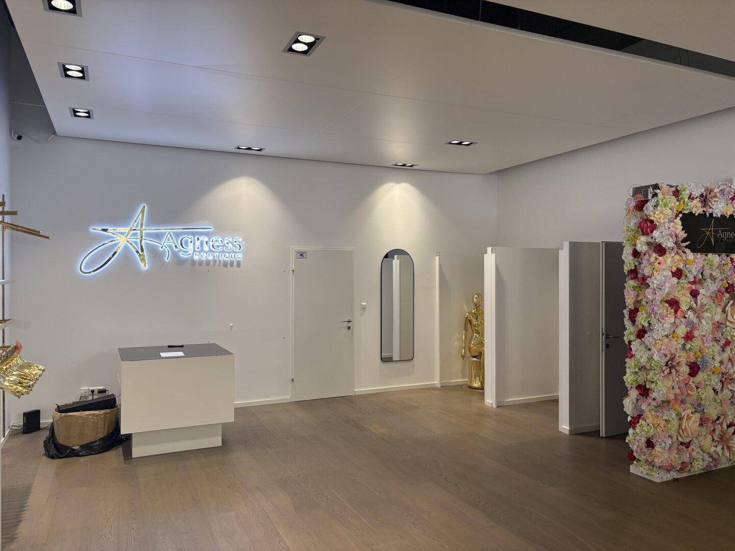 Heller Verkaufsraum einer Boutique mit Holzboden, Umkleidekabinen und einer dekorativen Blumenwand.