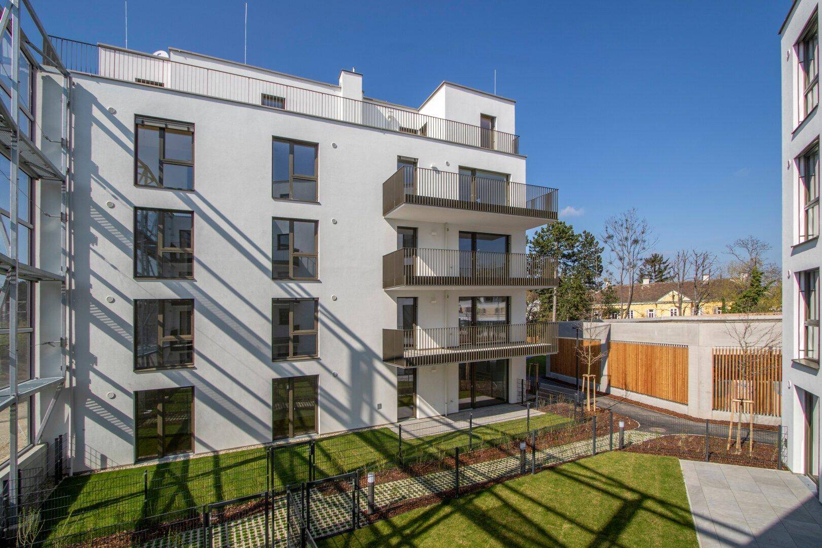 Ansicht eines modernen Wohngebäudes mit Balkonen und privaten Gartenbereichen im Erdgeschoss.