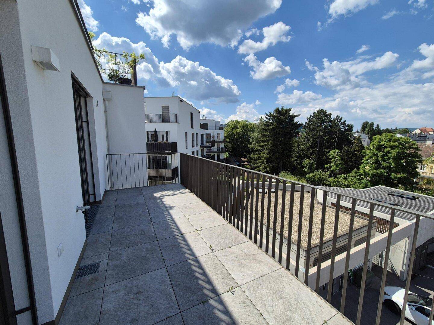 Großer Balkon mit Fliesenboden und Blick auf die umliegenden Gebäude und die grüne Landschaft.