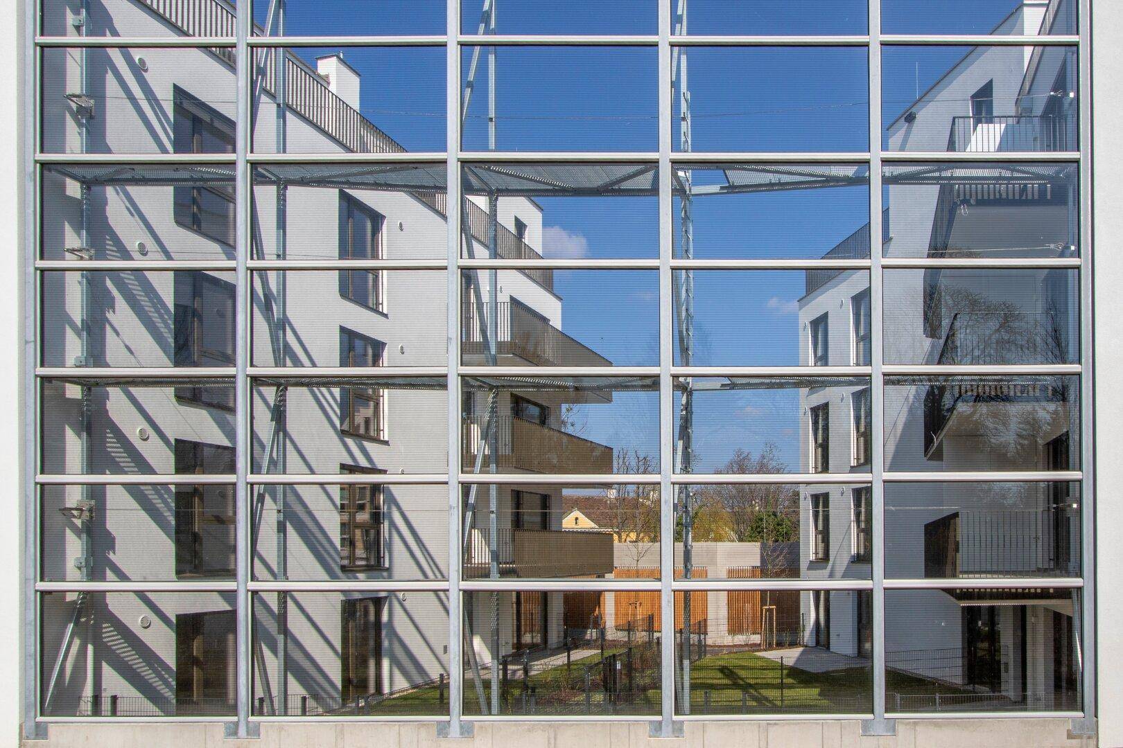 Reflektionen der modernen Wohngebäude in einer großen Glasfassade unter blauem Himmel.