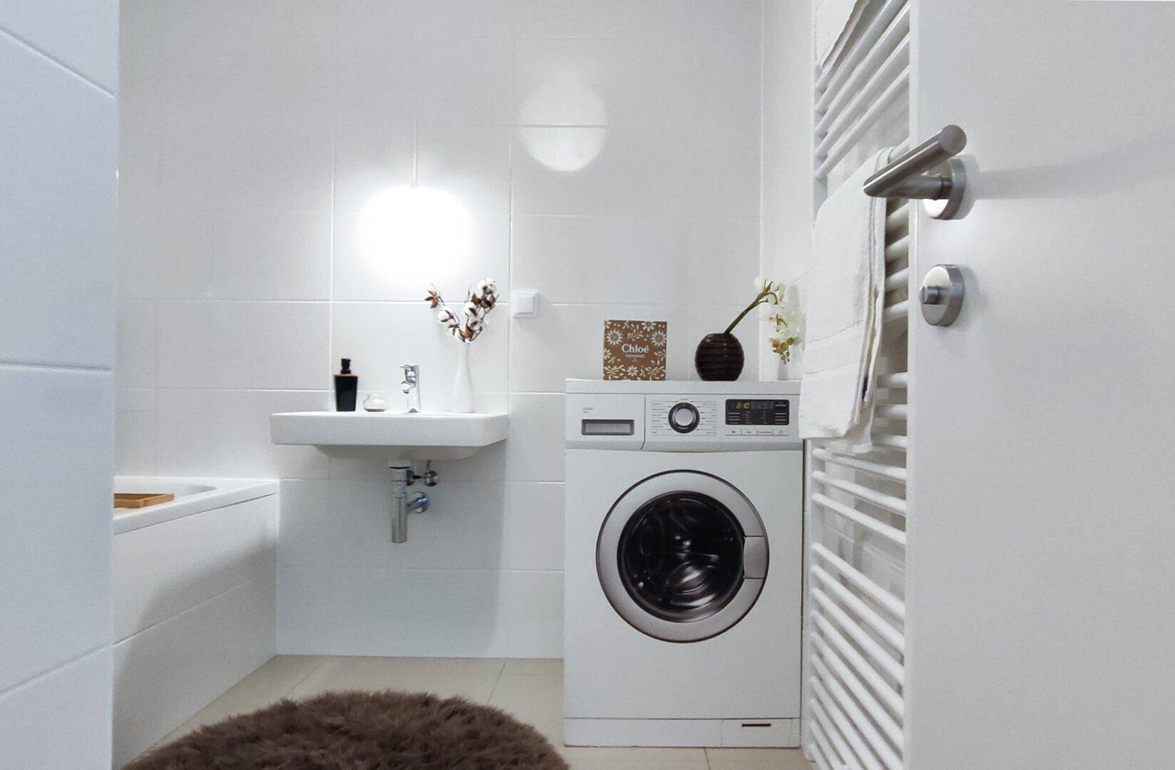 Modernes Badezimmer mit weißen Fliesen, Waschbecken, Badewanne und einer Waschmaschine.