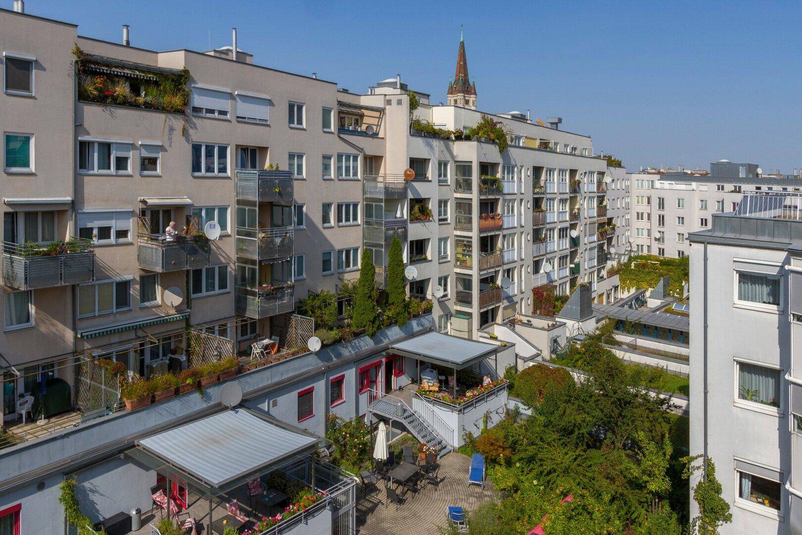 Luftaufnahme eines Wohnkomplexes mit vielen Balkonen, Terrassen und begrünten Innenhöfen.