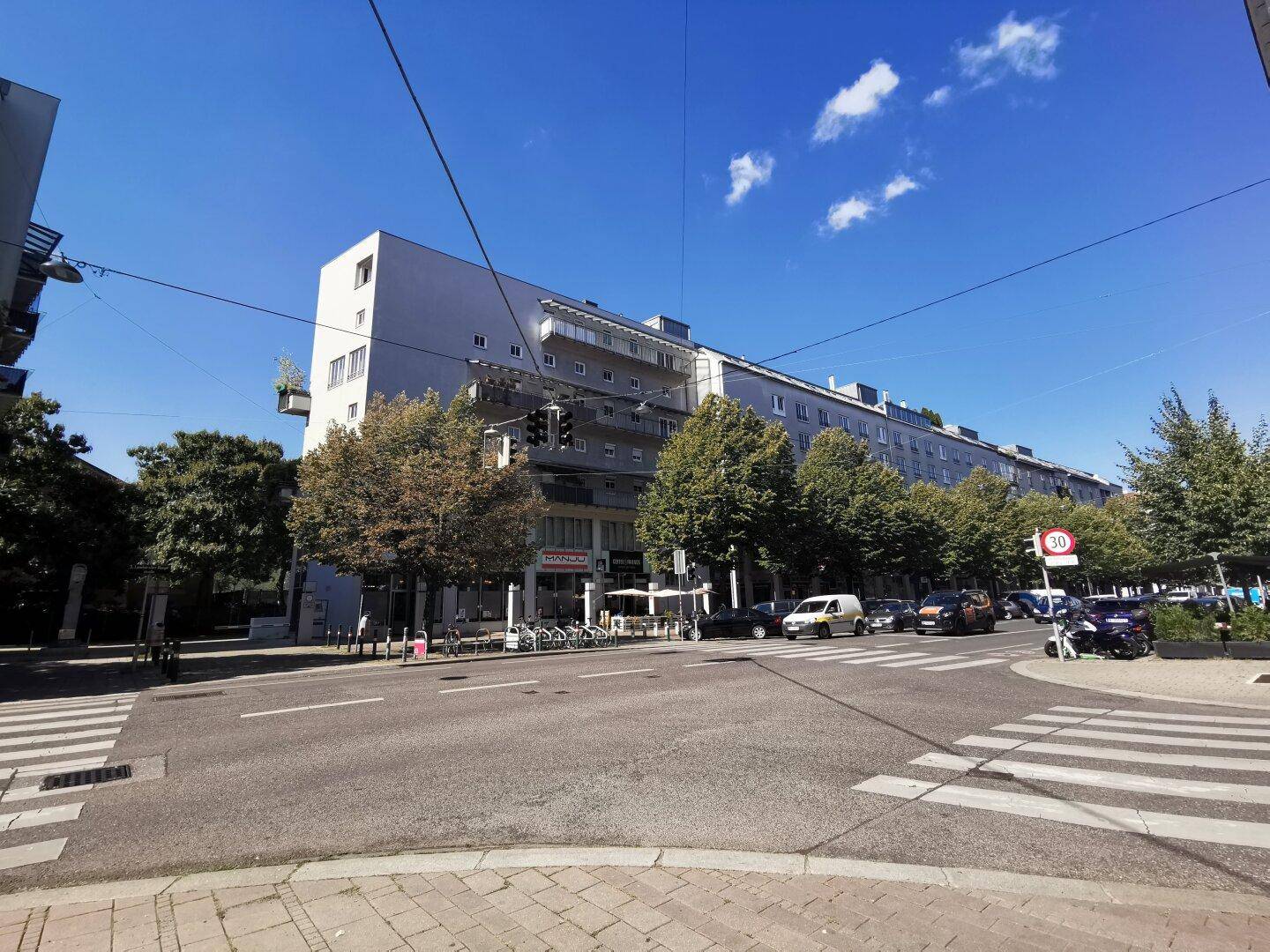Weitwinkelansicht eines großen Wohngebäudes an einer belebten Straße unter blauem Himmel.