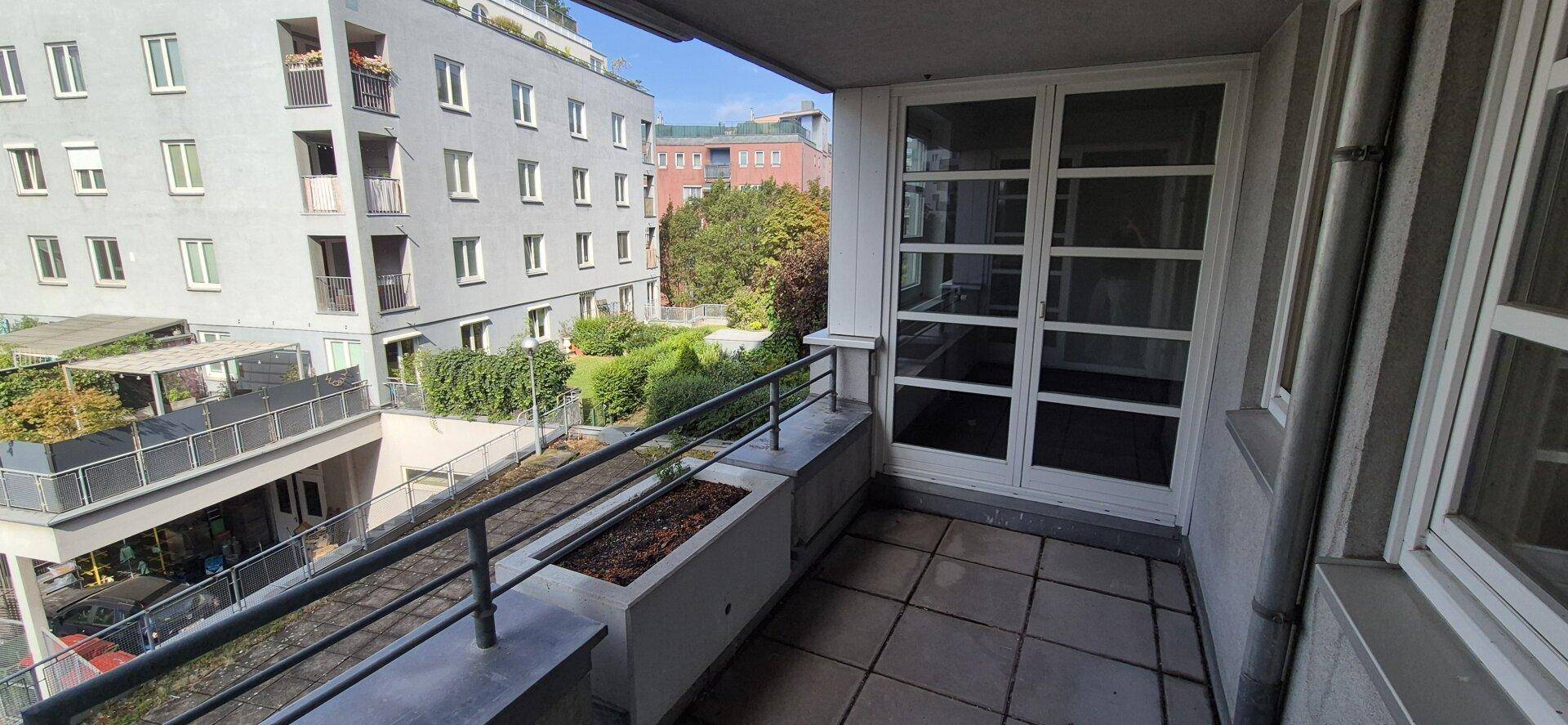 Balkon mit Fliesenboden und Metallgeländer, bietet Blick auf einen grünen Innenhof.