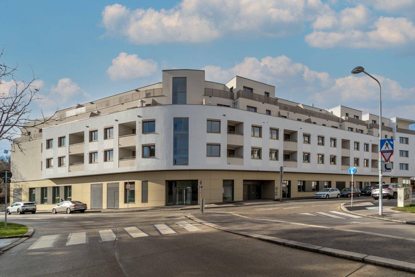 Ansicht des modernen Wohnkomplexes von der Straßenseite mit abgerundeten Ecken und vielen Fenstern.