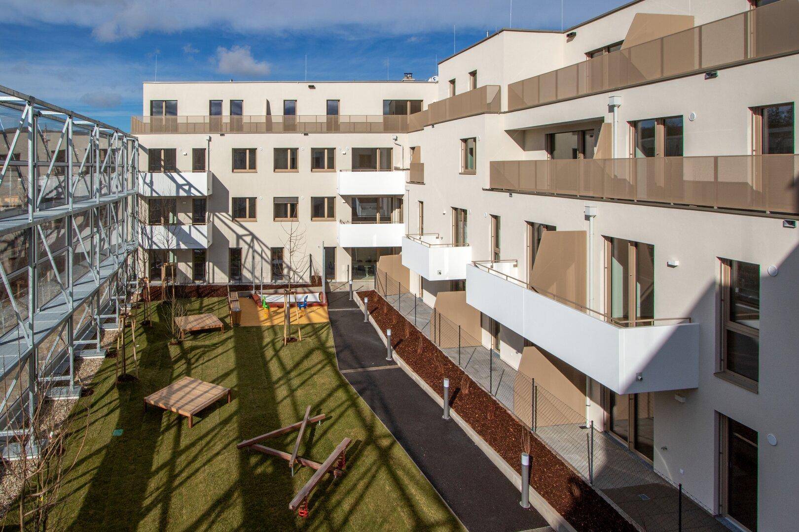 Innenhof des Wohnkomplexes mit Rasenfläche, Spielgeräten für Kinder und modernen Balkonen.