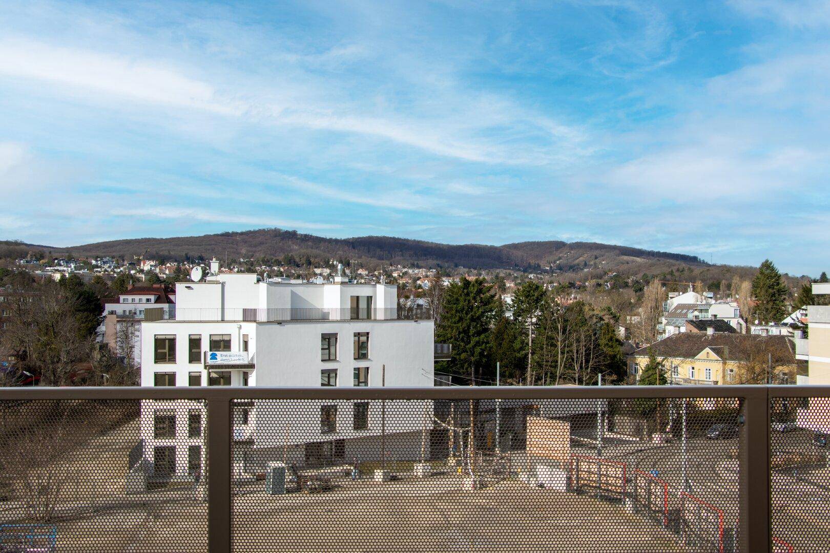 Weitläufiger Blick über die Stadt und die umliegende grüne Hügellandschaft von einem Balkon.