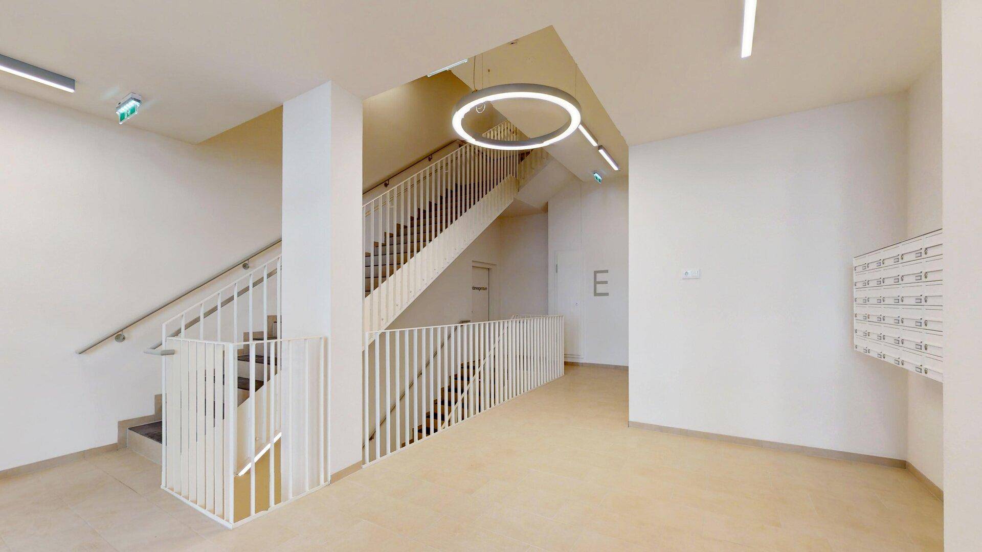 Heller und moderner Eingangsbereich mit Treppenhaus und Briefkästen in einem Neubau.