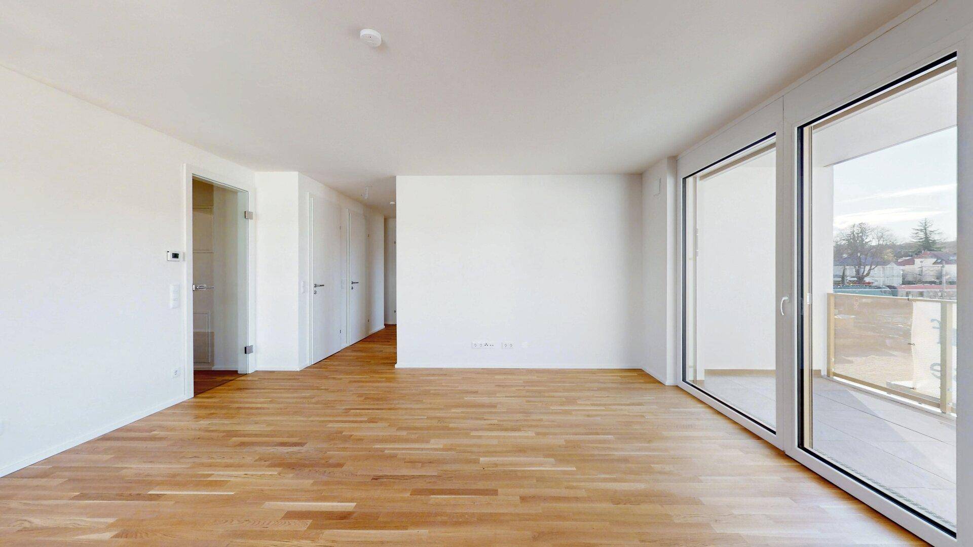 Geräumiges, helles Wohnzimmer mit Holzboden und Zugang zu einem Balkon oder einer Terrasse.