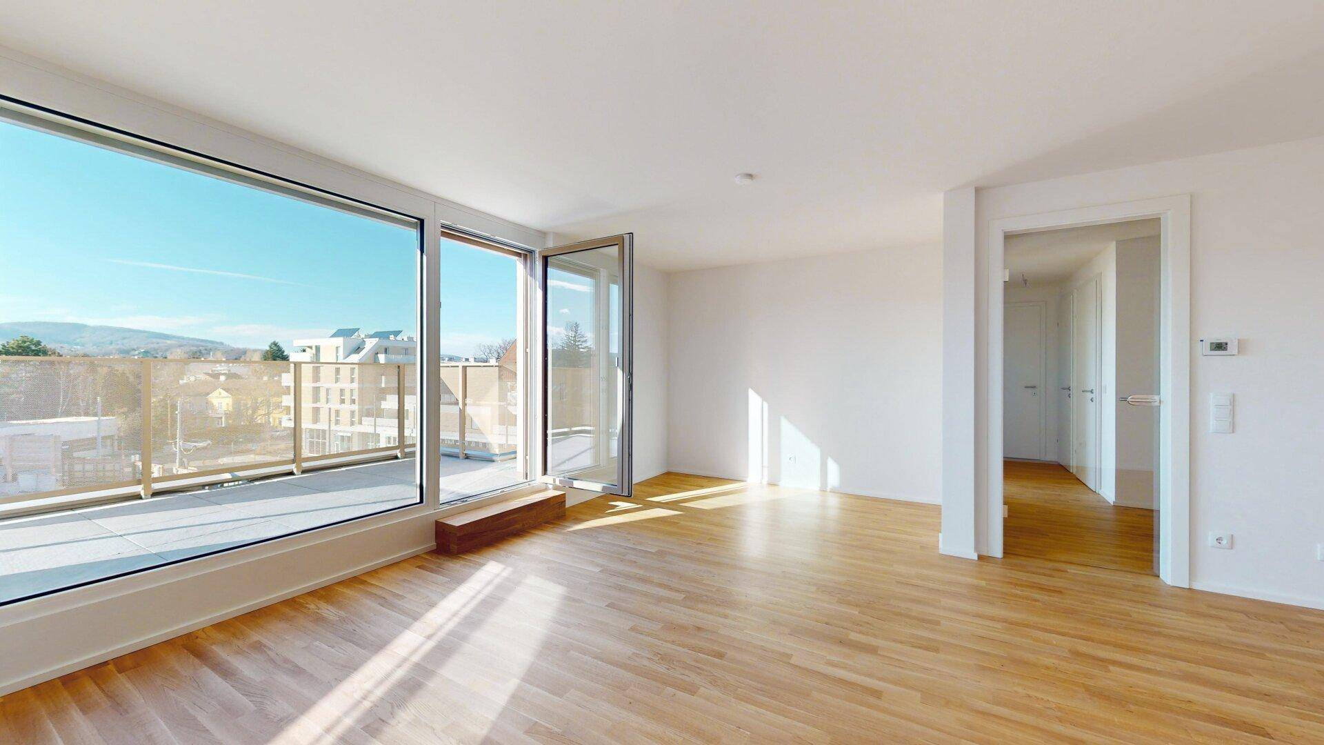 Lichtdurchflutetes Wohnzimmer mit Eichenparkett und großen Fenstern, die auf einen Balkon führen.
