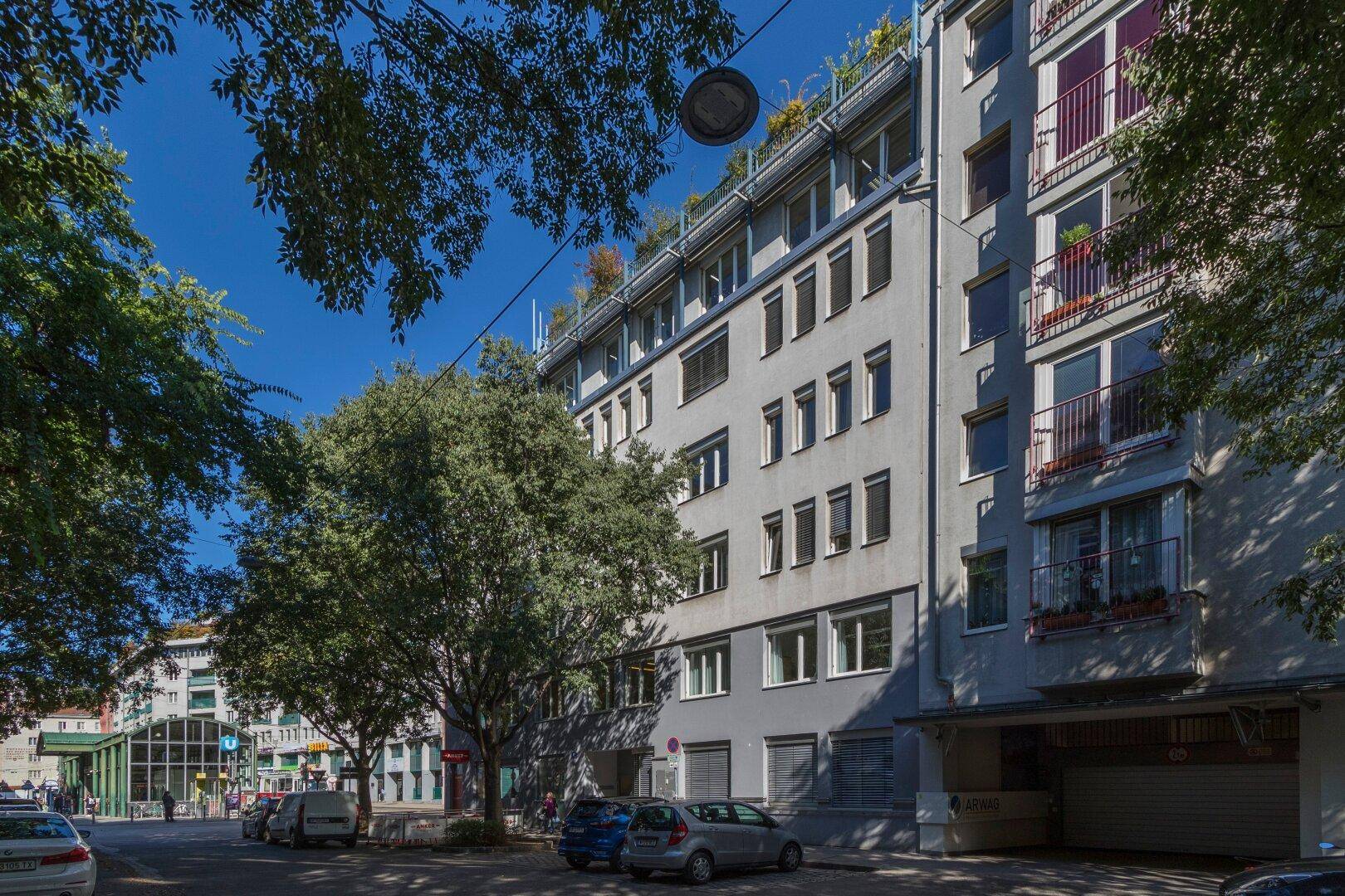 Ansicht eines modernen Wohngebäudes mit vielen Fenstern und begrüntem Dach in städtischer Umgebung.