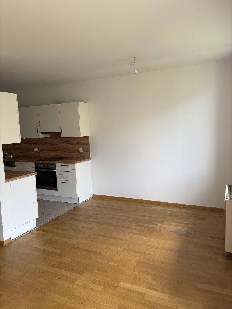 Heller offener Wohnbereich mit integrierter Küche, Parkettboden und weißen Wänden.