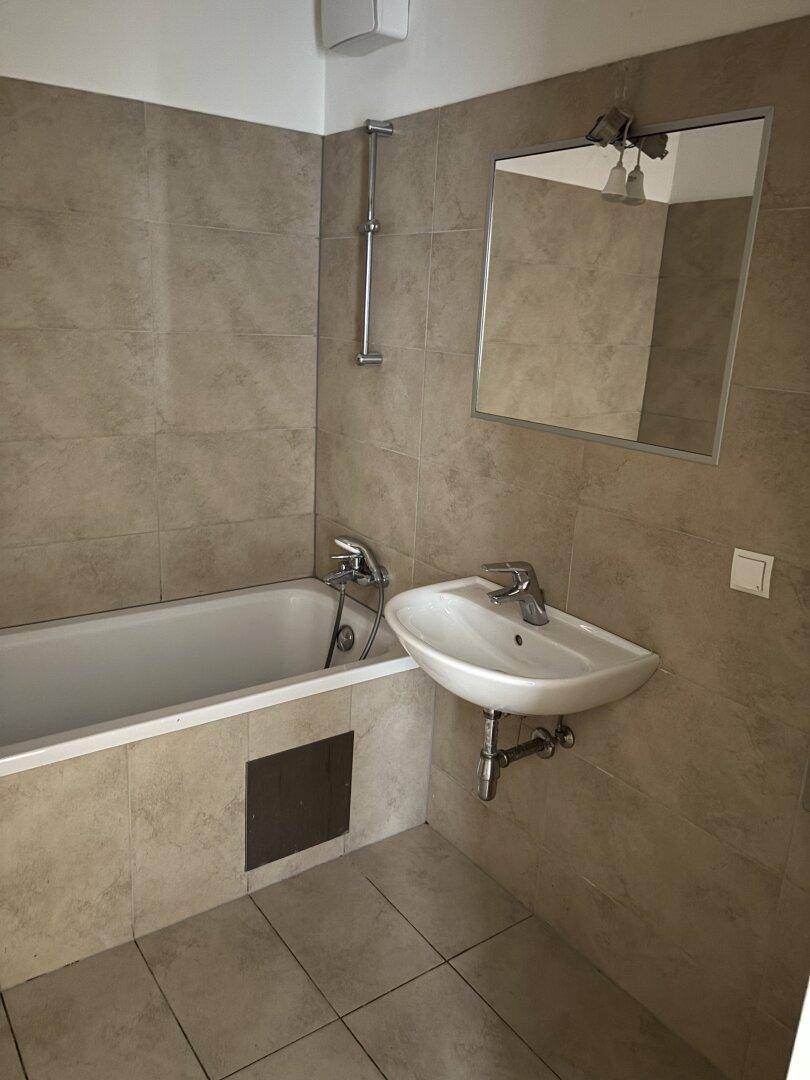 Modernes Badezimmer mit beigefarbenen Fliesen, Badewanne und einem einzelnen Waschbecken.