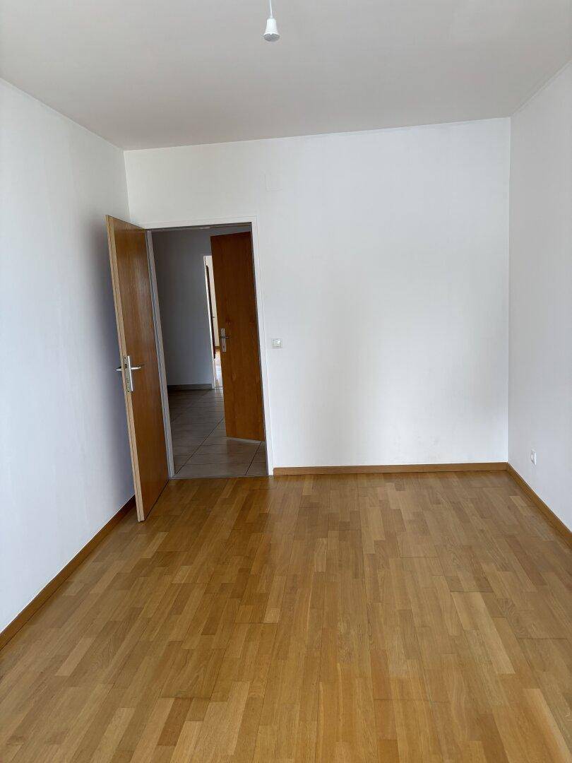 Leeres Zimmer mit hellem Parkettboden, weißen Wänden und Holztüren.