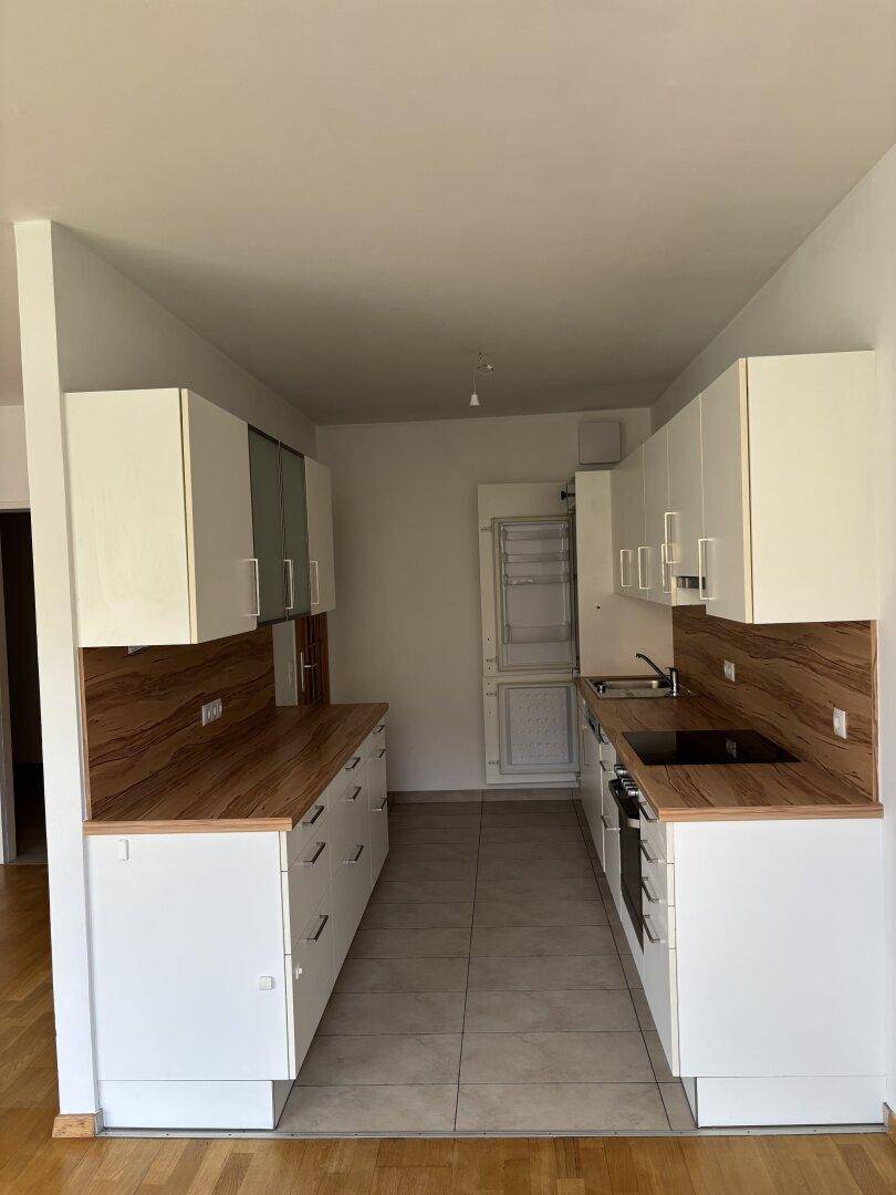 Funktionale Küche mit weißen Schränken, Holzoptik-Arbeitsplatten und Fliesenboden.