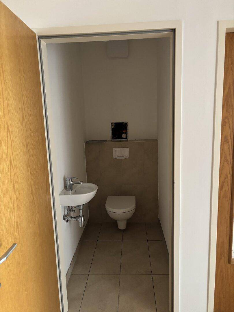 Kleines Gäste-WC mit Wand-WC, kleinem Waschbecken und Fliesenboden.