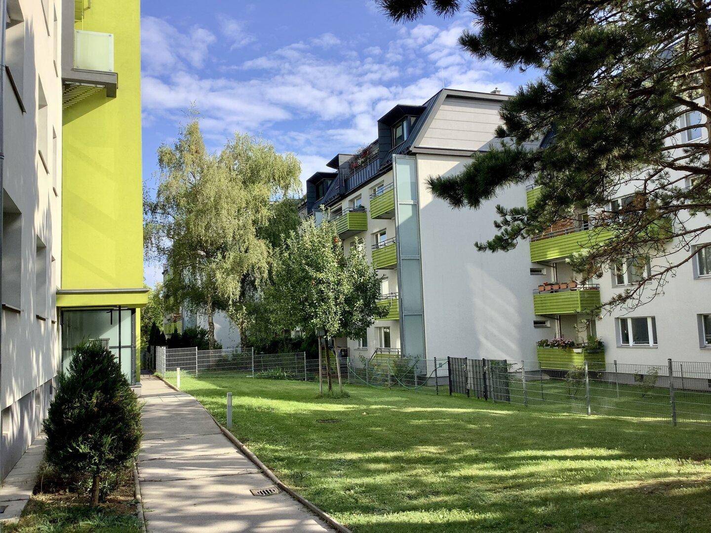 Gepflegte Grünfläche mit Bäumen und Gehwegen zwischen den modernen Wohngebäuden.