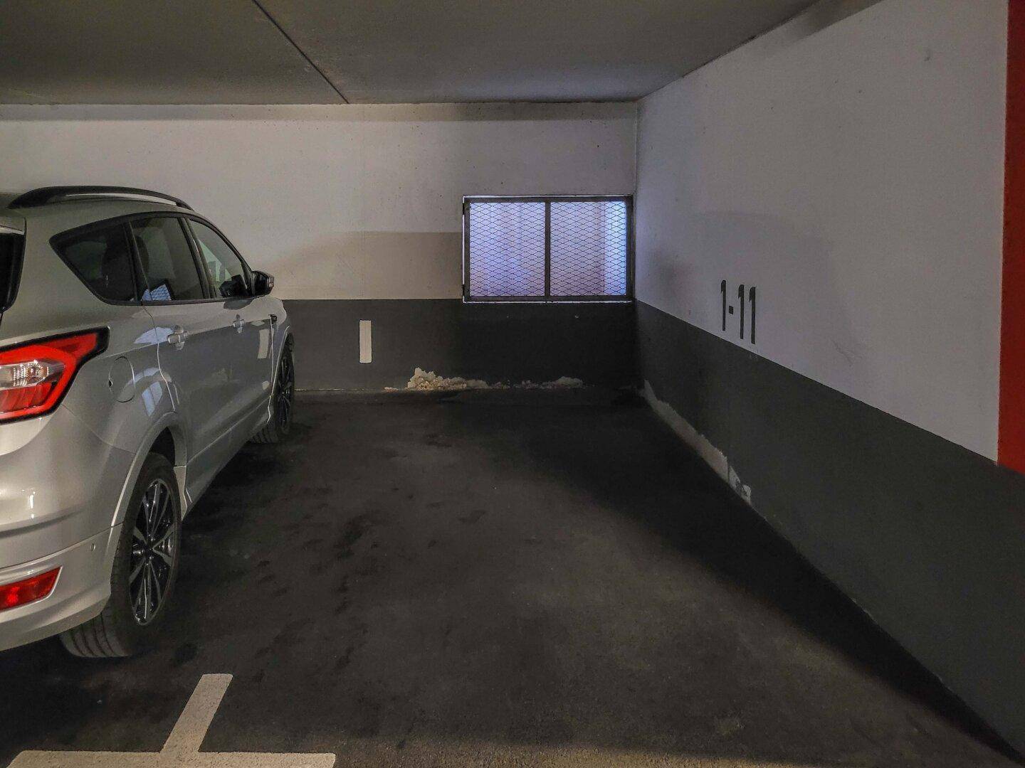Tiefgaragenstellplatz mit einem silbernen Fahrzeug und einem kleinen vergitterten Fenster im Hintergrund.