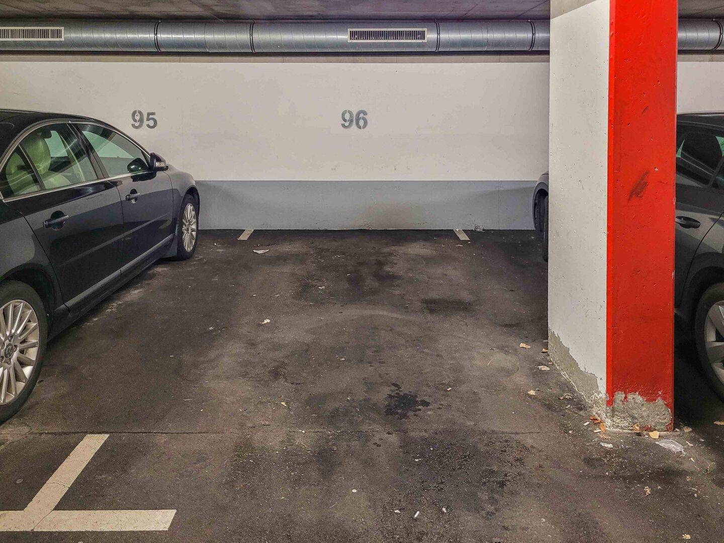 Leerer Parkplatz in der Tiefgarage zwischen zwei geparkten Fahrzeugen, mit Nummerierung.