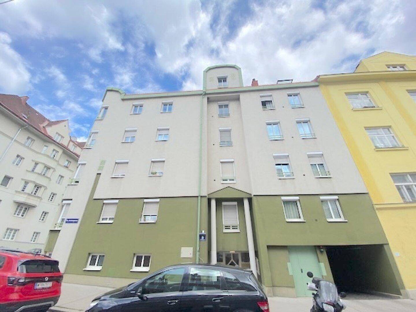 Mehrstöckiges Wohngebäude mit grün-beiger Fassade und Rollläden an den Fenstern.