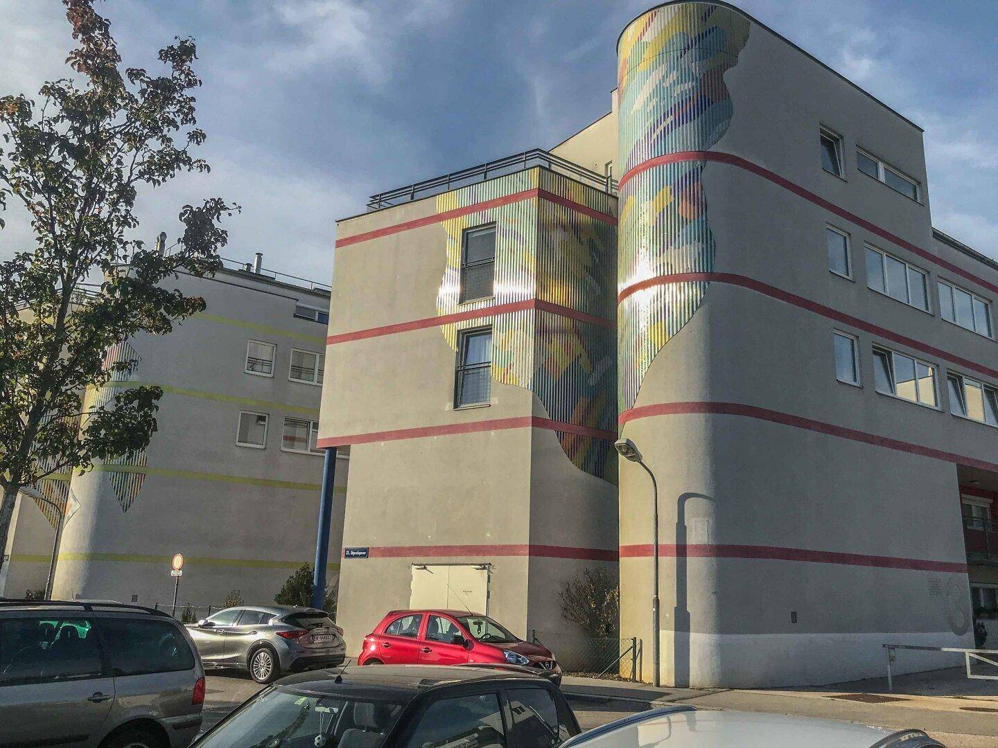 Moderne Wohngebäude mit farbenfrohen Fassadenelementen und großen Fenstern unter blauem Himmel.