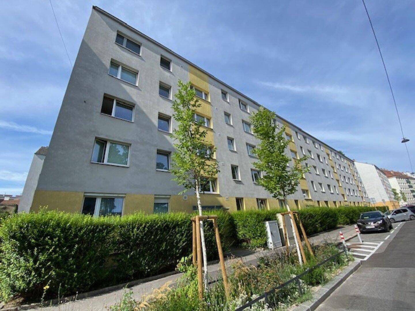 Mehrstöckiges Wohngebäude mit moderner Architektur, grauer und gelber Fassade sowie gepflegter Grünanlage.