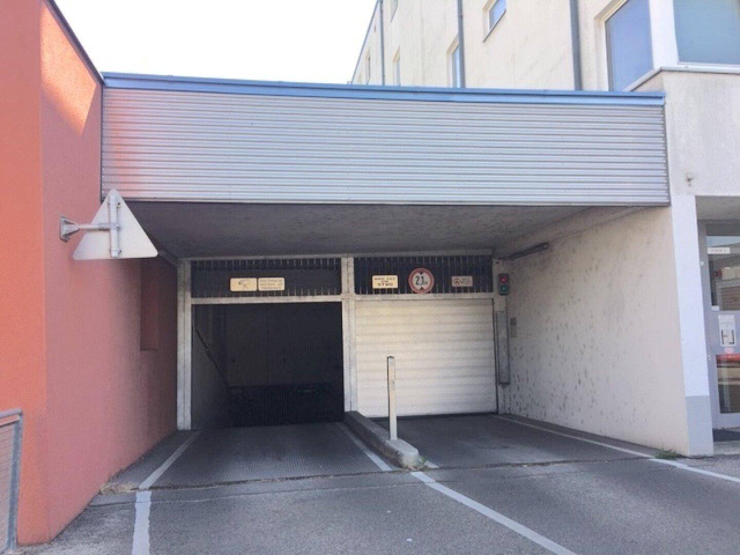 Einfahrt zur Tiefgarage mit Rampe und Rolltor, gekennzeichnet durch Höhenbeschränkung und Hinweisschilder.