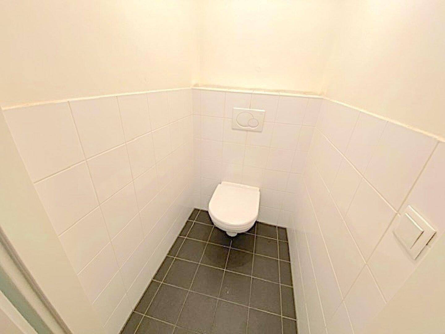 Kleines Gäste-WC mit weißen Fliesen an den Wänden und dunklen Bodenfliesen.