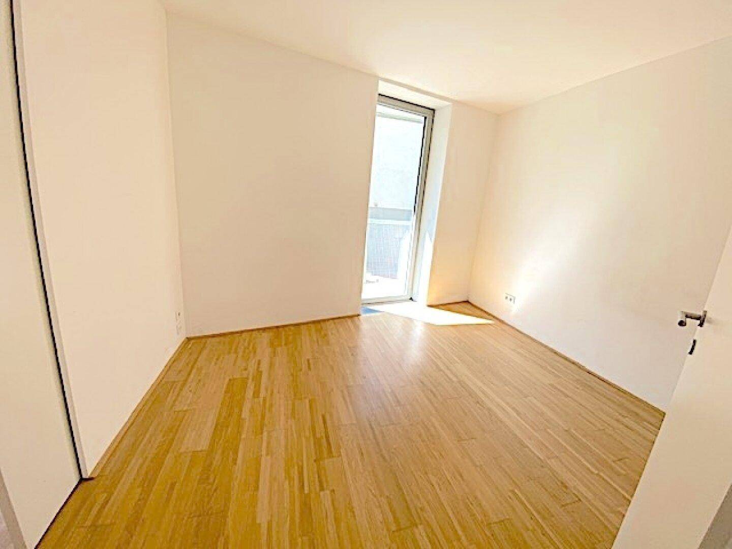 Helles Schlafzimmer mit Holzboden und einem Fenster, das viel Tageslicht in den Raum bringt.