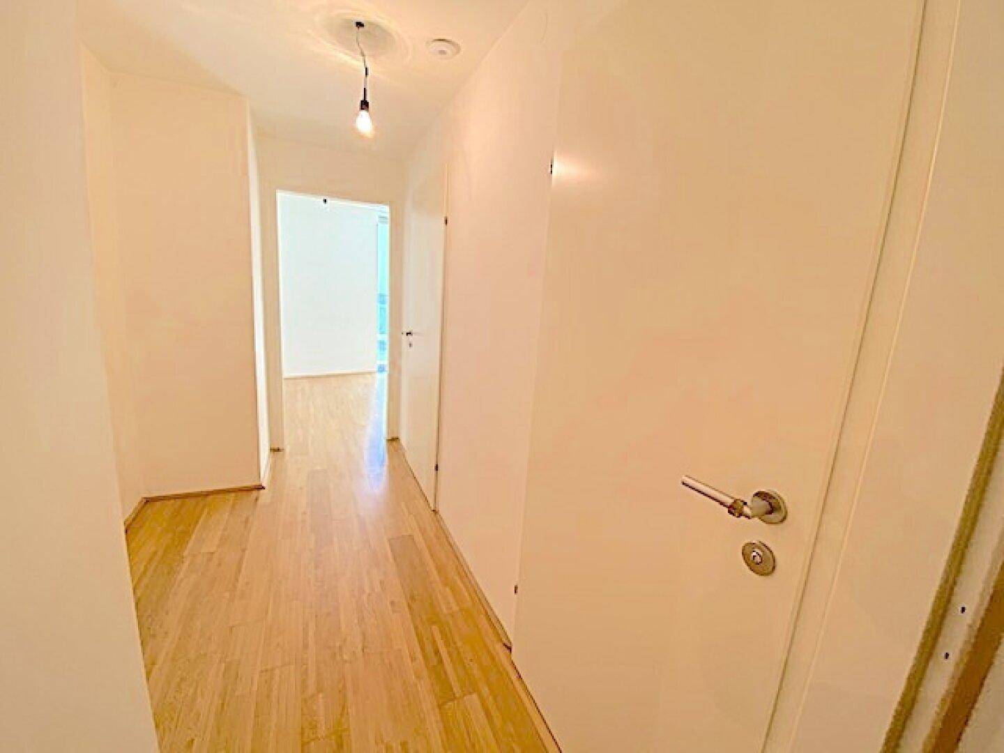 Heller Flur mit Holzboden und weißen Türen, der zu verschiedenen Räumen der Wohnung führt.