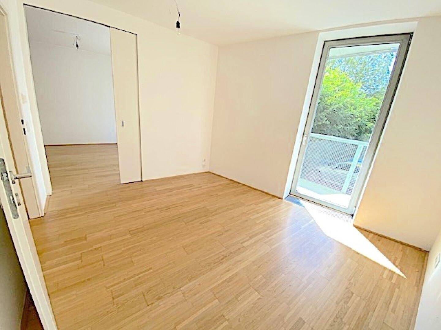 Leerer, heller Raum mit Holzboden und einem großen, schrägen Fenster, das viel Tageslicht hereinlässt.