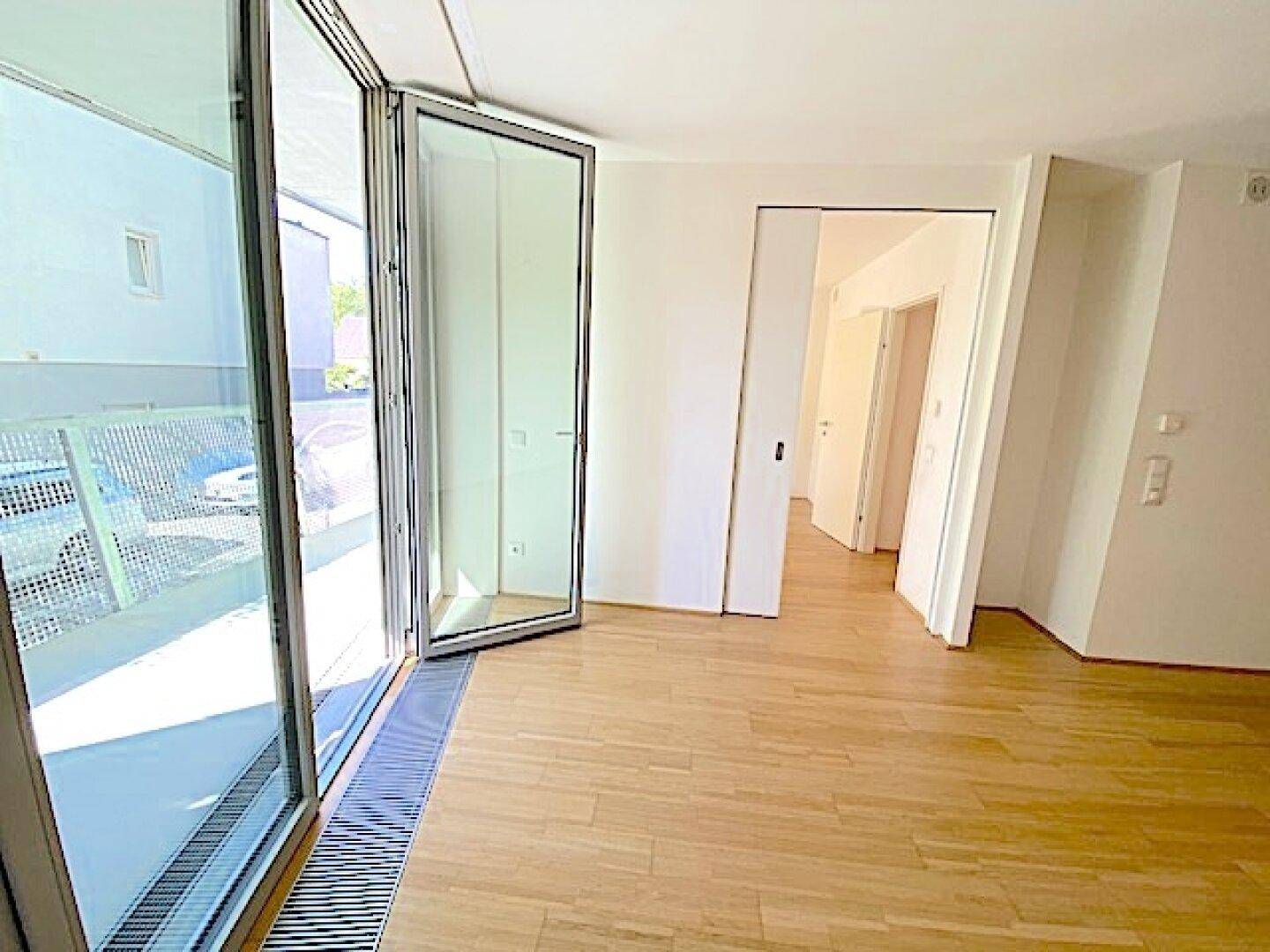 Heller Wohnbereich mit Holzboden und großer Glasfront, die Zugang zu einem sonnigen Balkon bietet.