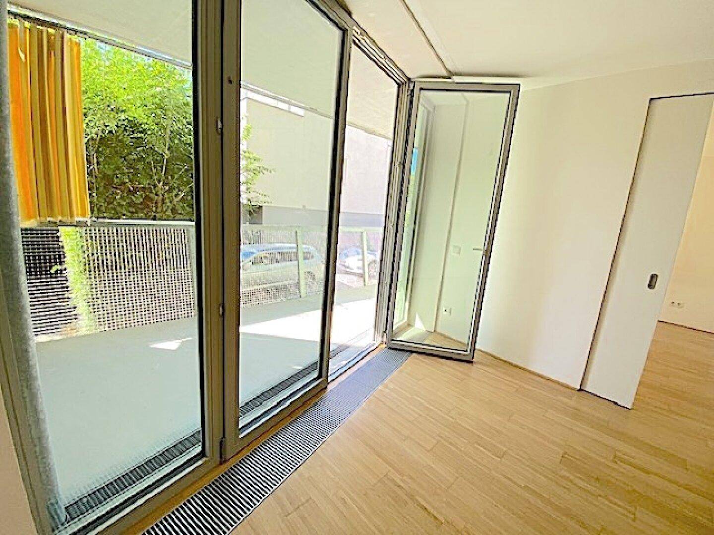 Wohnbereich mit Holzboden und großer Glasfront, die sich zu einem sonnigen Balkon öffnen lässt.