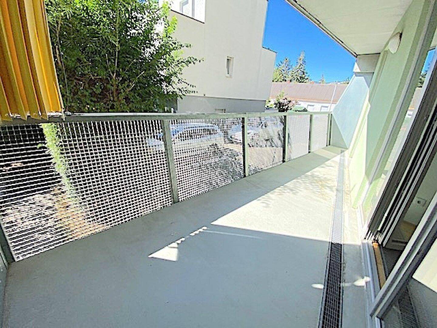 Langer Balkon mit modernem Metallgeländer und Blick auf die grüne Umgebung an einem sonnigen Tag.