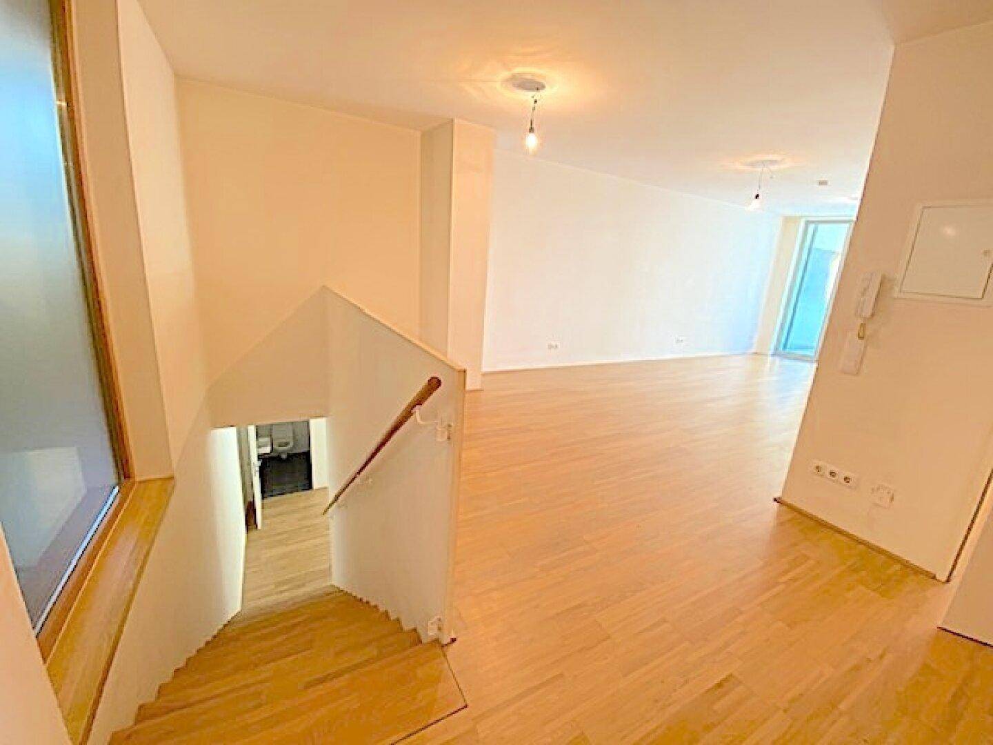 Geräumiger Wohnbereich mit Holzboden und einer Treppe, die in eine untere Etage führt.