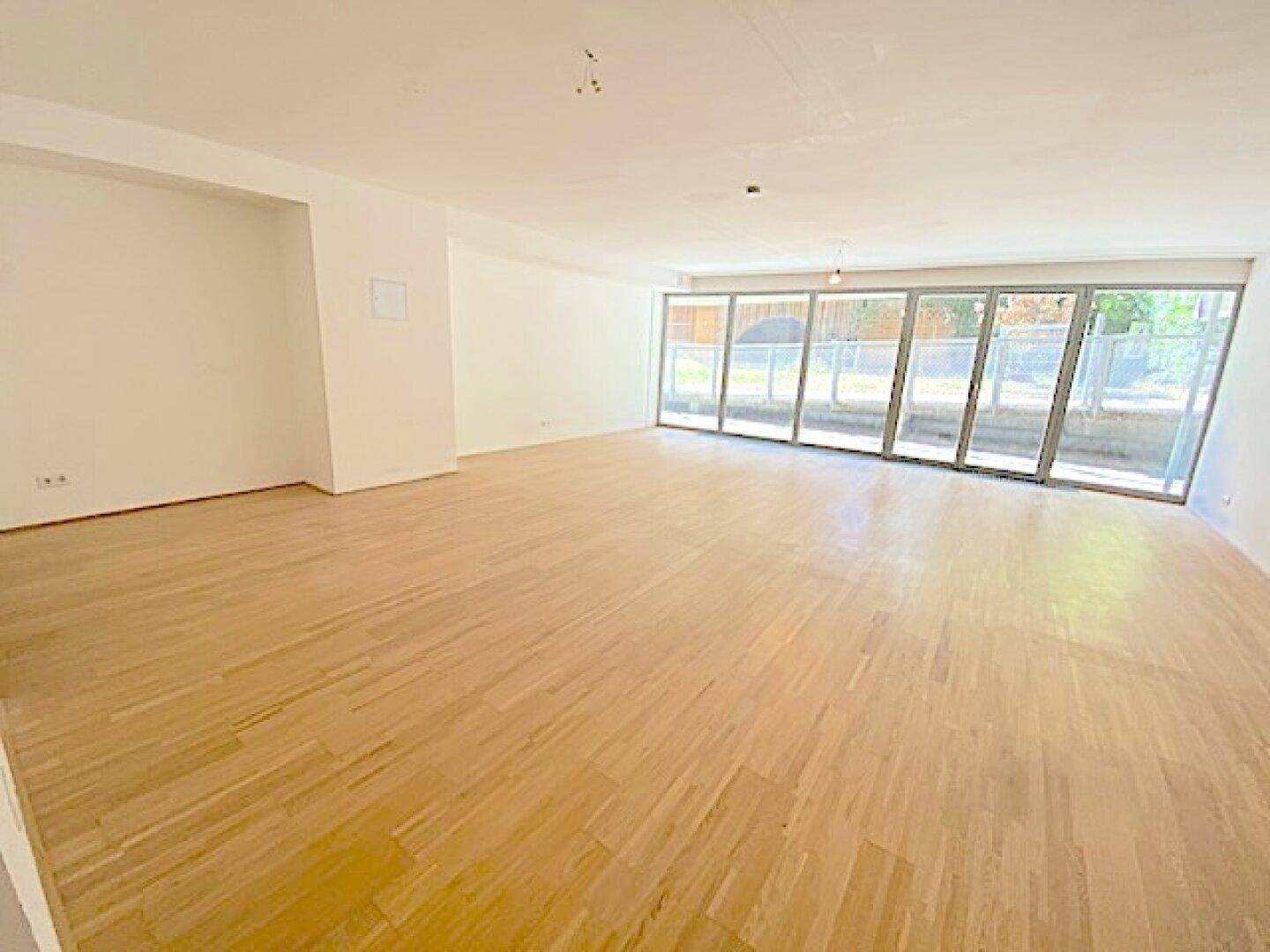 Großer, heller Wohnbereich mit Holzboden und einer breiten Fensterfront, die viel Licht spendet.