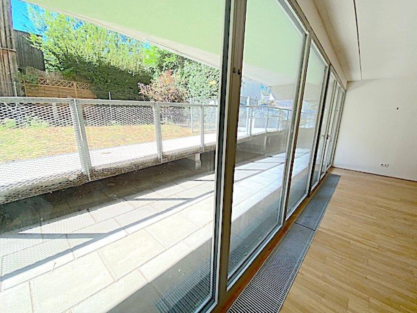 Wohnbereich mit Holzboden und großer Glasfront, die Zugang zu einer Terrasse oder einem Garten bietet.