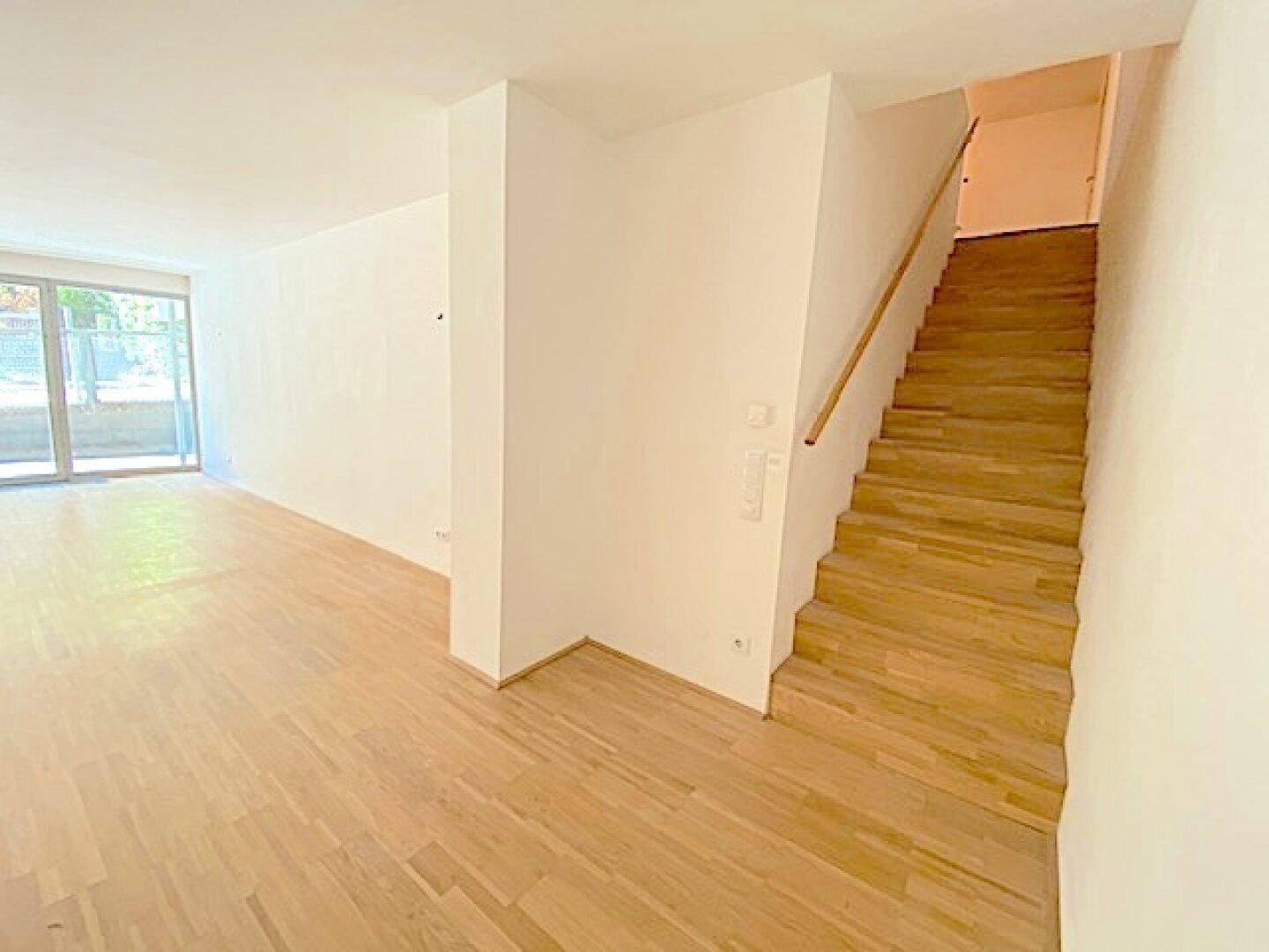 Heller Wohnbereich mit Holzboden und einer Holztreppe, die in die obere Etage führt.