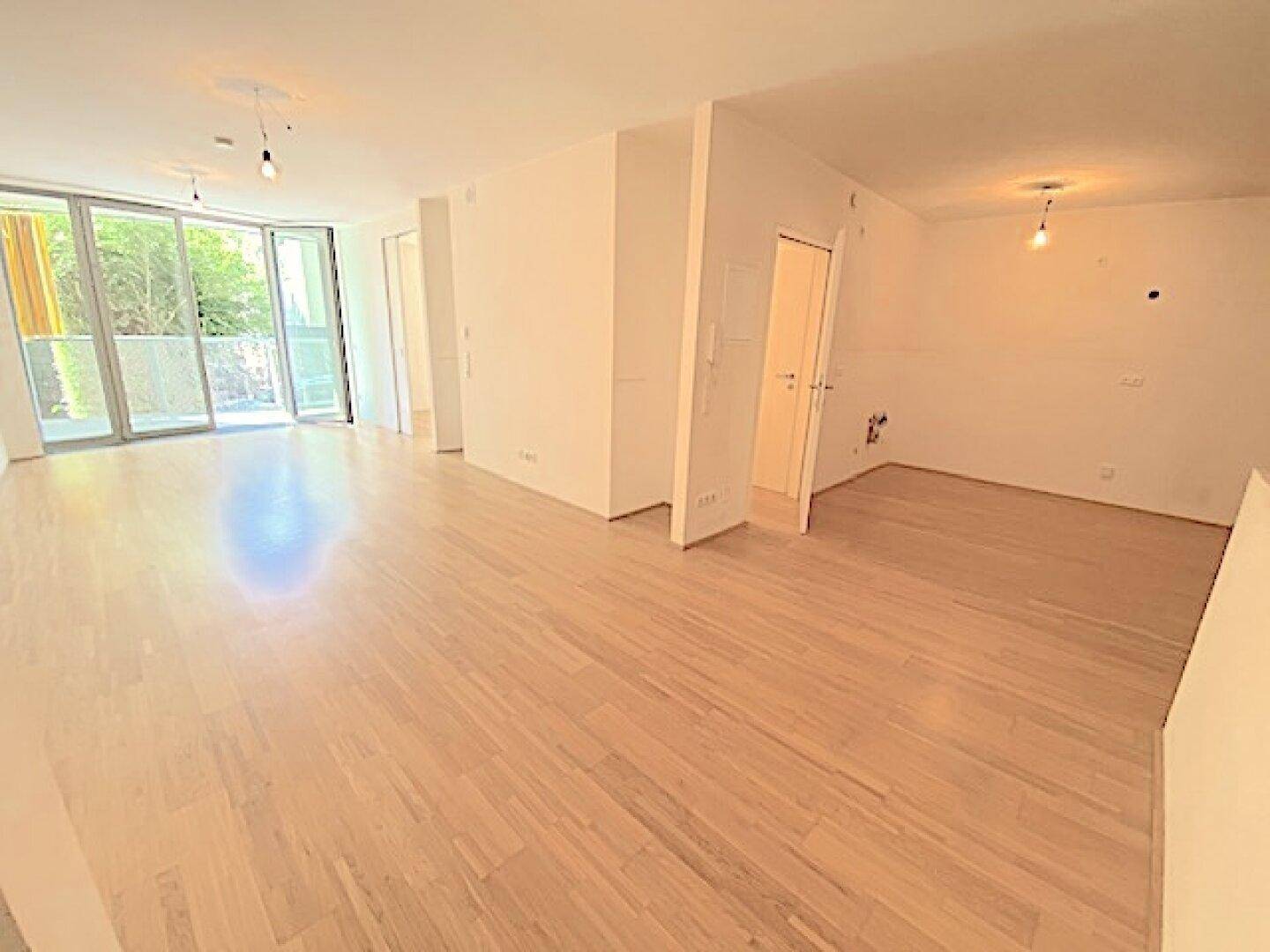Geräumiger, heller Wohnbereich mit Holzboden und großen Fenstern, die viel Tageslicht hereinlassen.