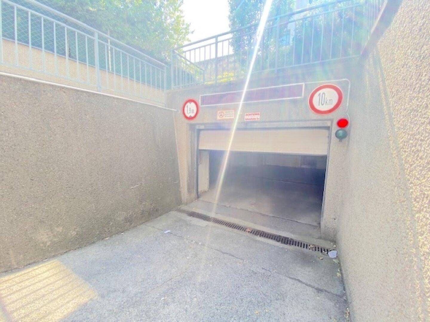 Einfahrt zu einer Tiefgarage mit Rampe und Verkehrsschildern, umgeben von Betonwänden.