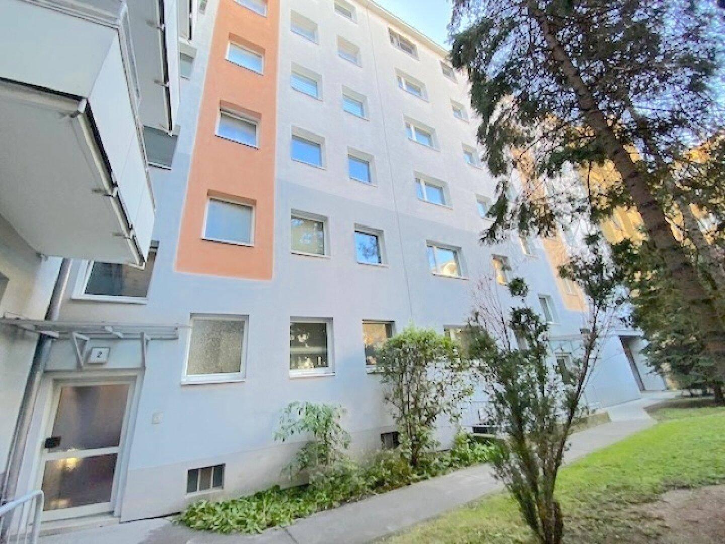 Außenansicht eines Mehrfamilienhauses mit weißer Fassade und grüner Umgebung.