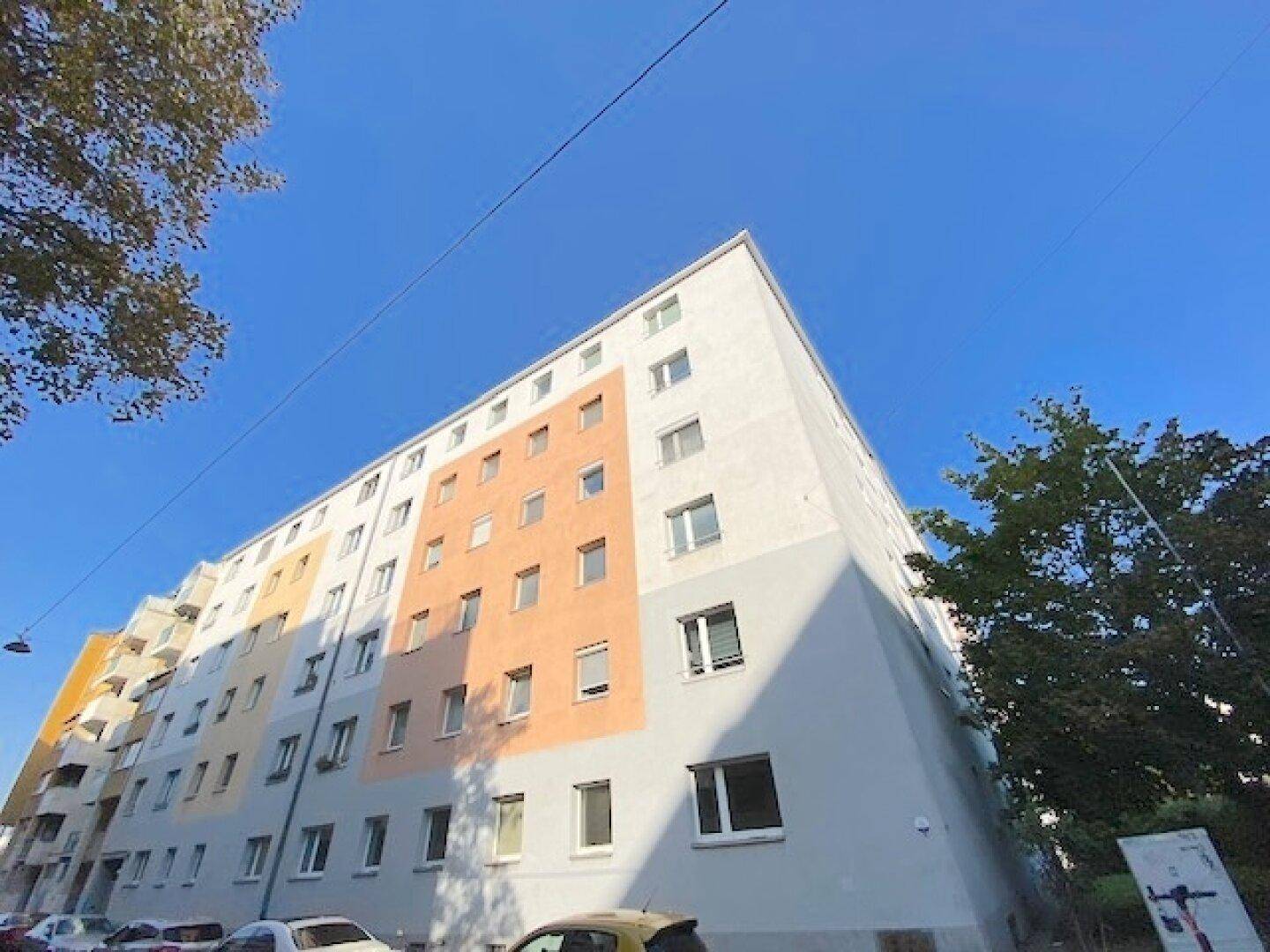 Mehrstöckiges Wohngebäude mit farbigen Fassadenabschnitten unter blauem Himmel.