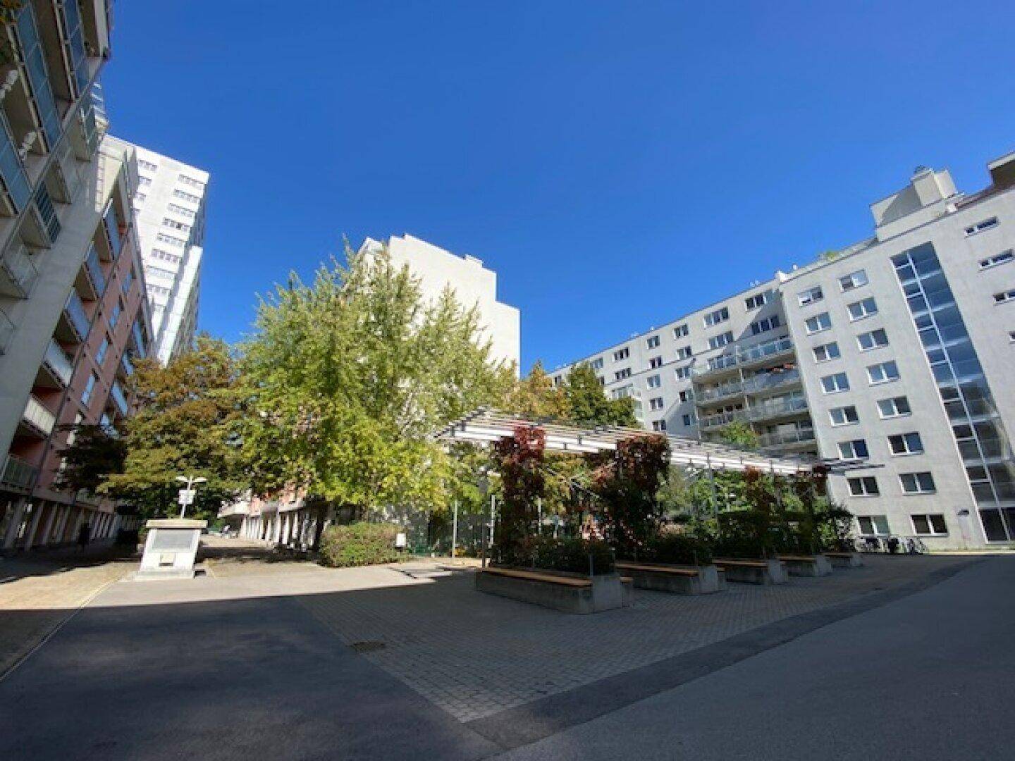 Moderne Wohngebäude mit grüner Innenhofgestaltung und Sitzgelegenheiten unter einer Pergola.