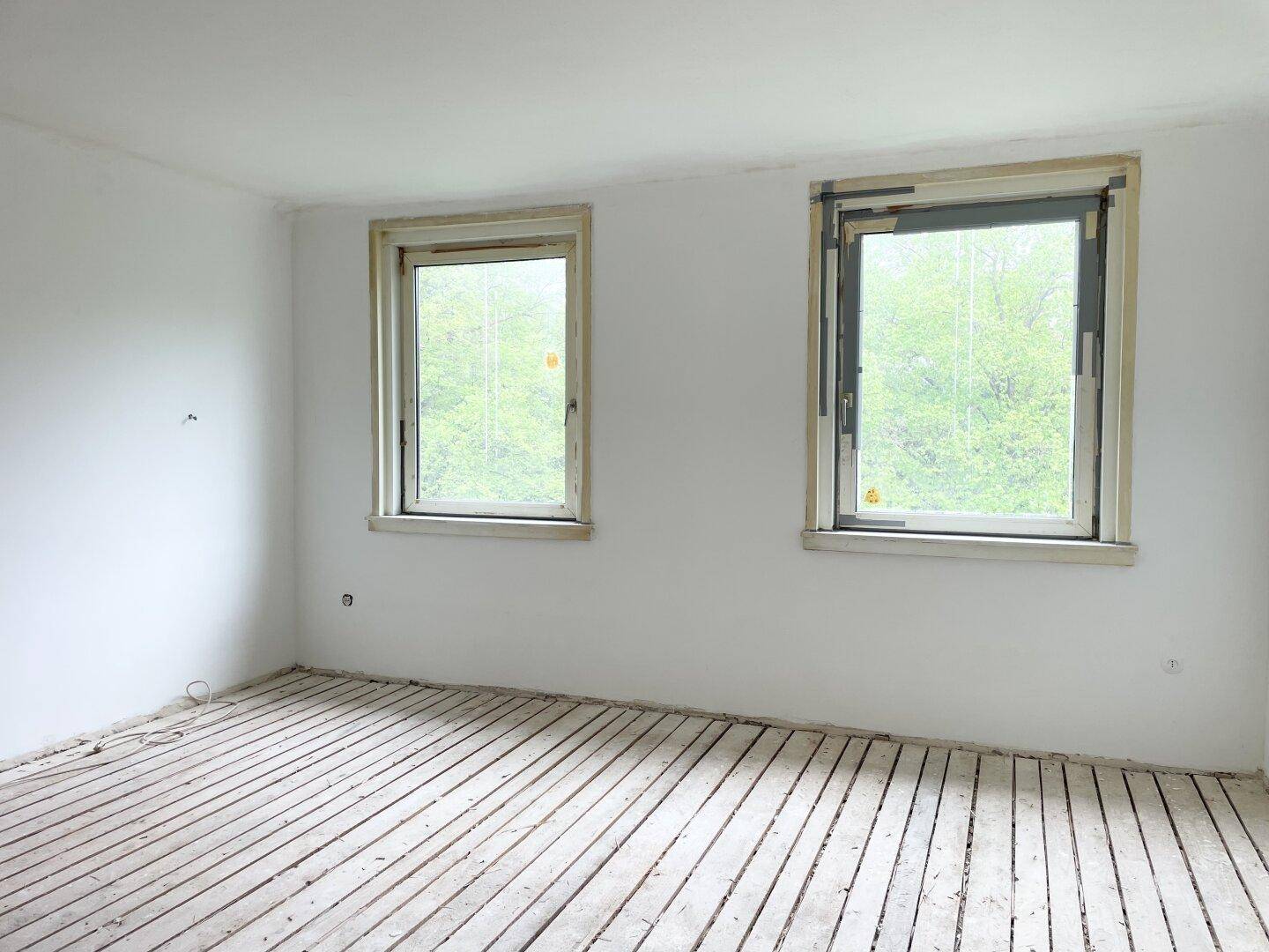 Heller Raum mit zwei Fenstern und Blick auf Bäume, bereit für die weitere Renovierung.
