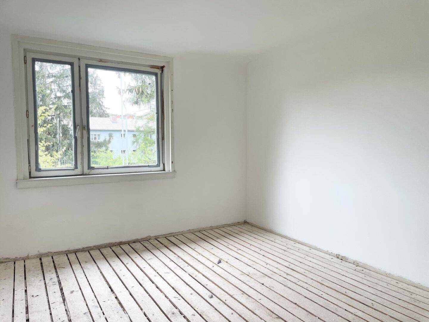 Leerer Raum mit einem Fenster, das einen Blick auf Bäume und ein entferntes Gebäude freigibt.