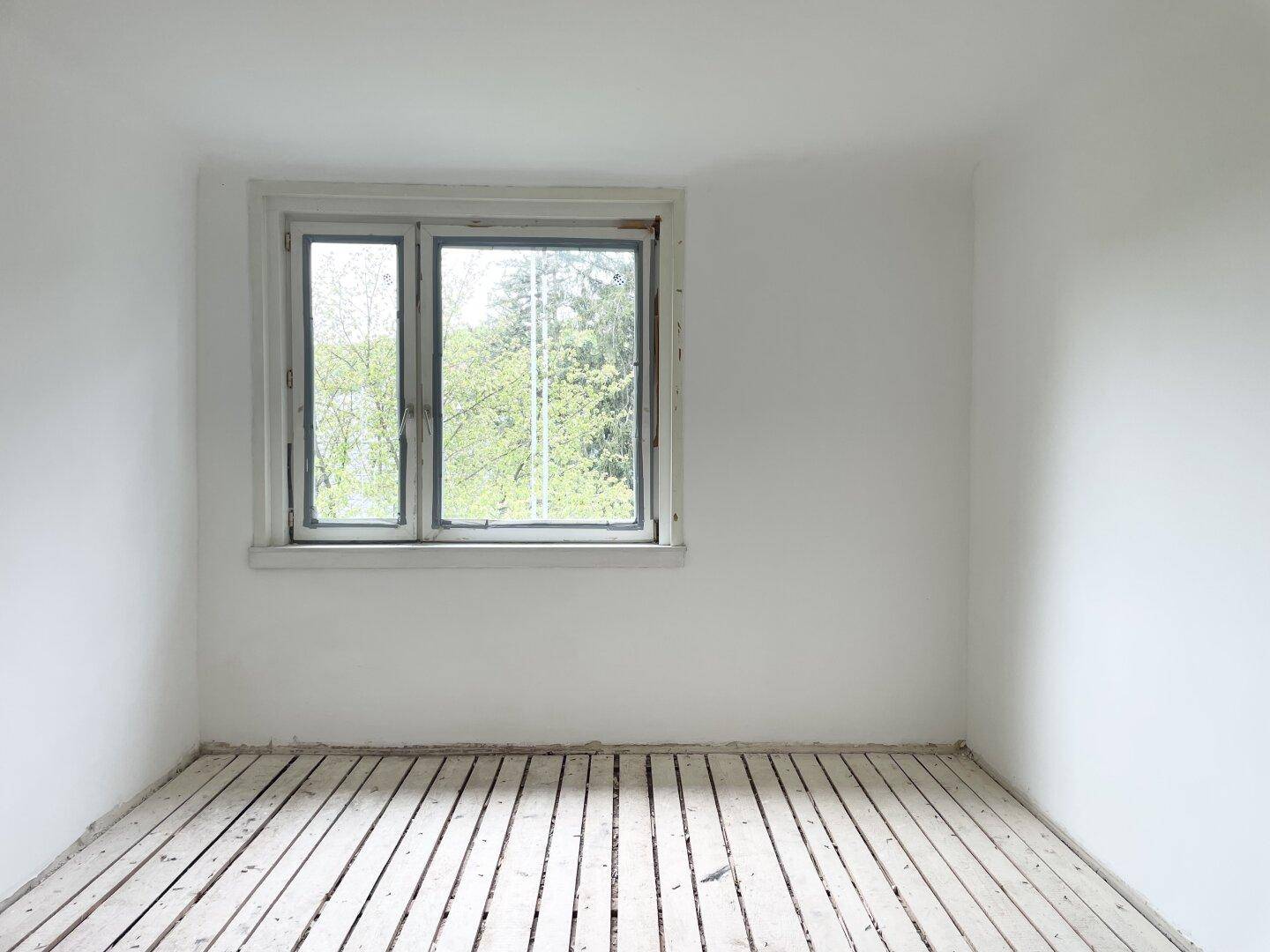 Heller Raum mit einem Fenster, das viel Tageslicht hereinlässt und einen Blick ins Grüne bietet.
