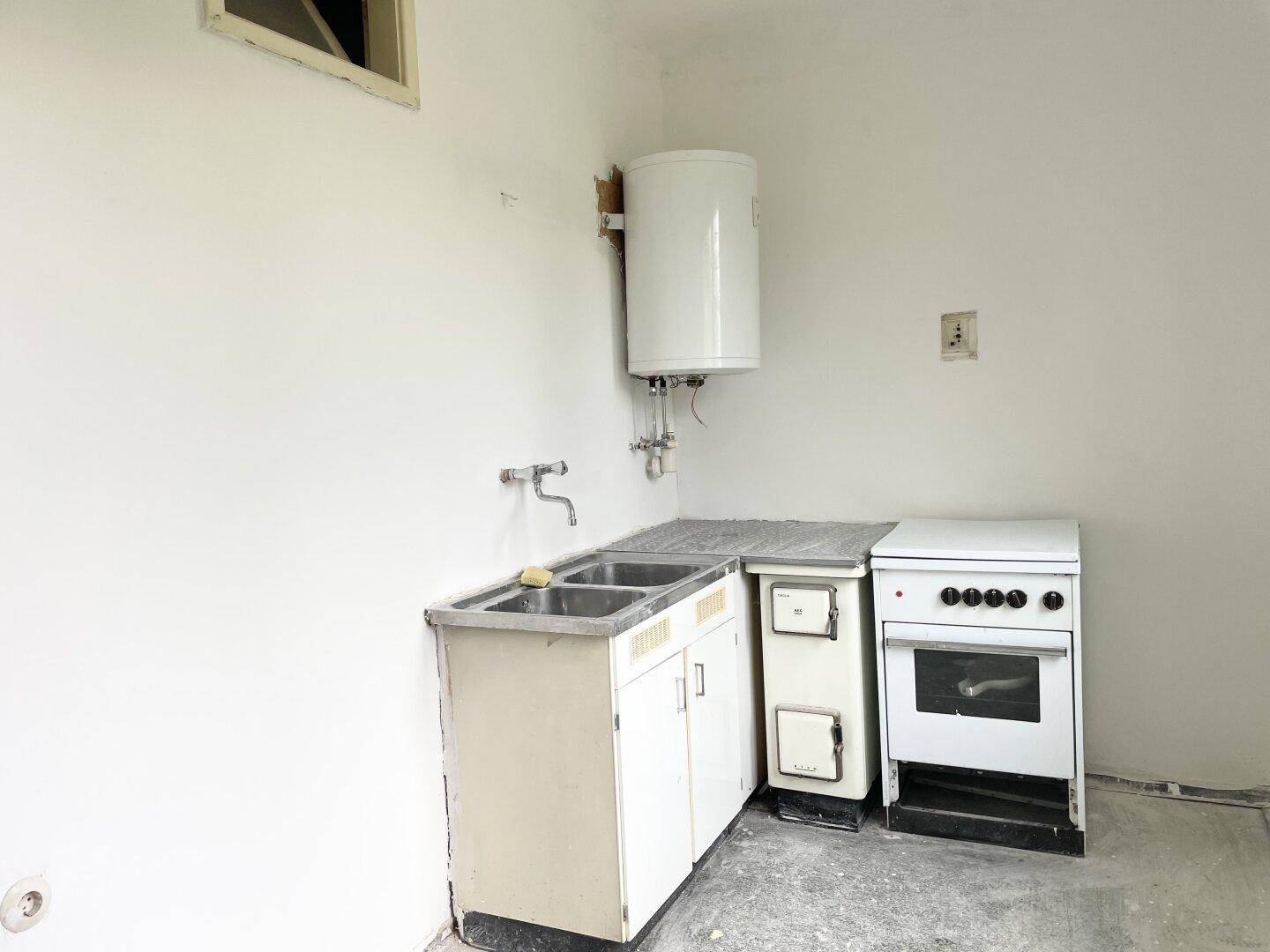 Einfache Küche mit Spüle, Boiler und freistehendem Herd, bereit für eine Modernisierung.
