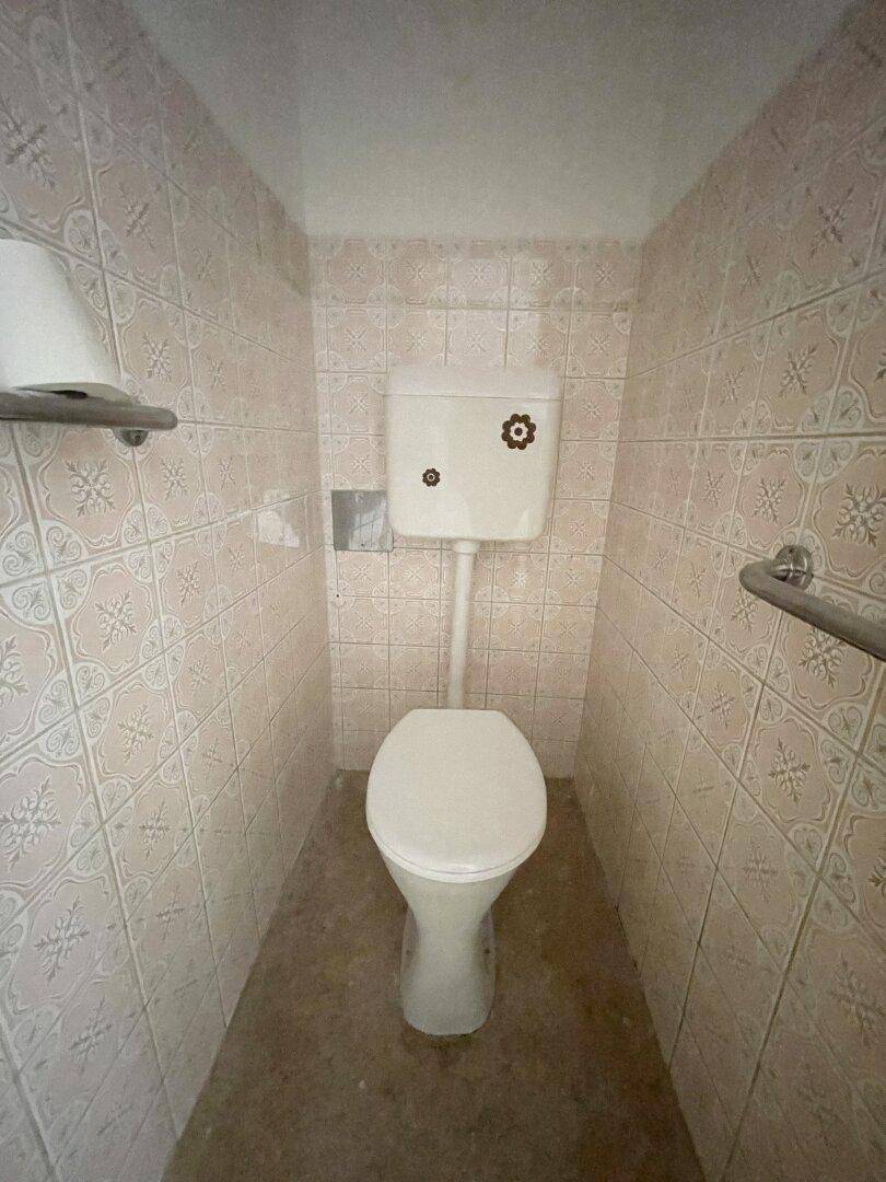 Kleines WC mit hellrosa gemusterten Fliesen und einer Toilette.